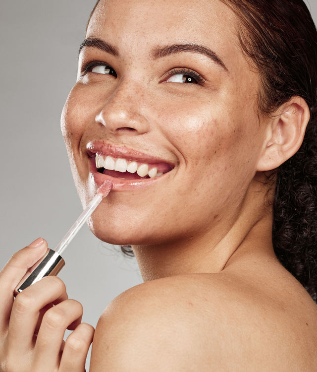 Beauty Shopify theme Beautify. Woman applying lip balm to her lips with a gray background.