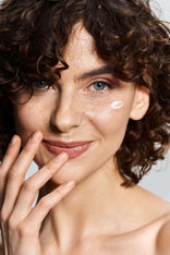 Beauty Shopify Theme Beautify Woman_with_a_light_cream_product_on_her_cheek_against_a_neutral_background.